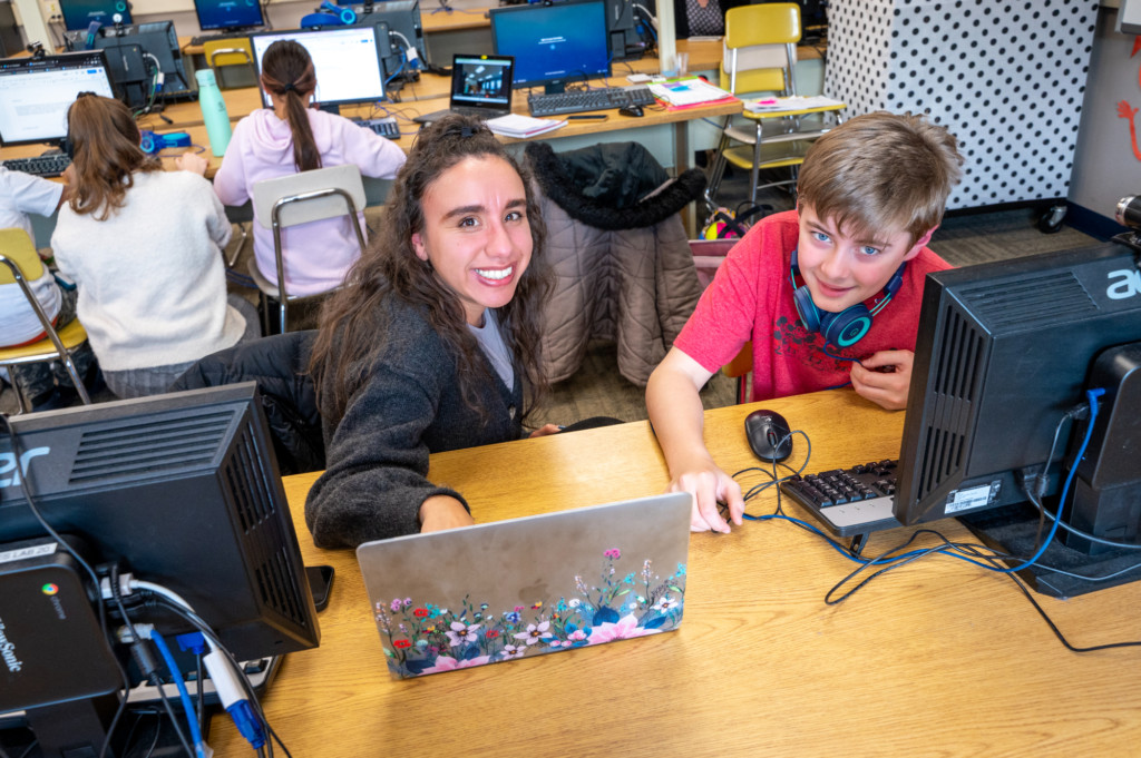 student teacher and elementary student at laptop in classroom