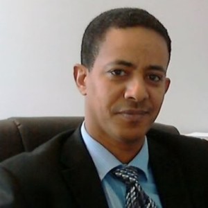 man in dark suit with light blue shirt and tie.