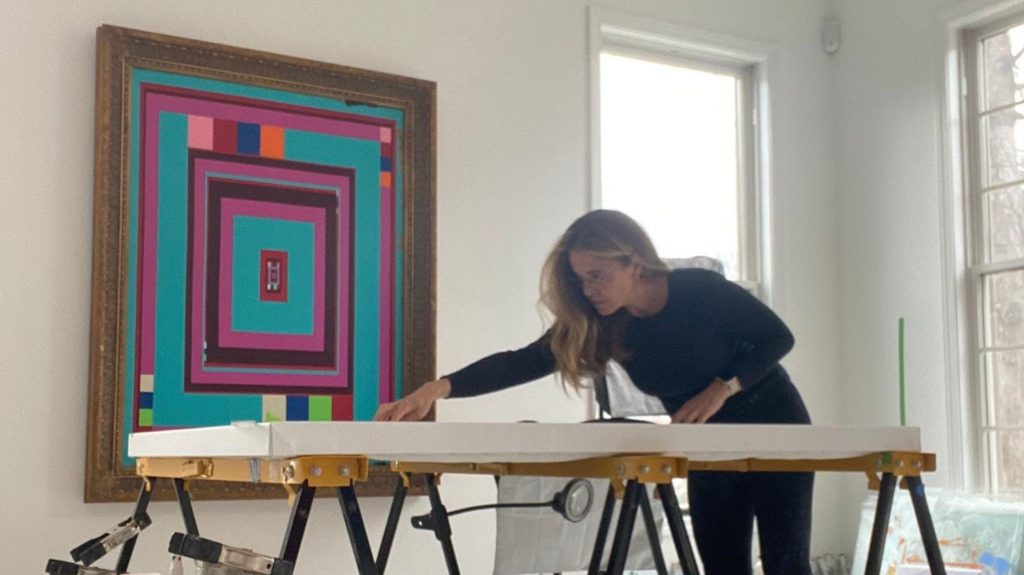 Artist Michelle Bowen working in her studio; "Real and Fake Inside News" hangs in the background.