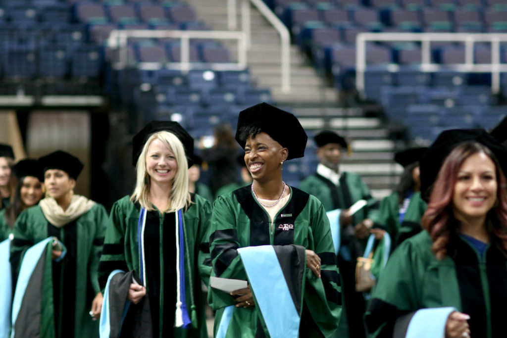 Three smiling graduates in green gowns walking
