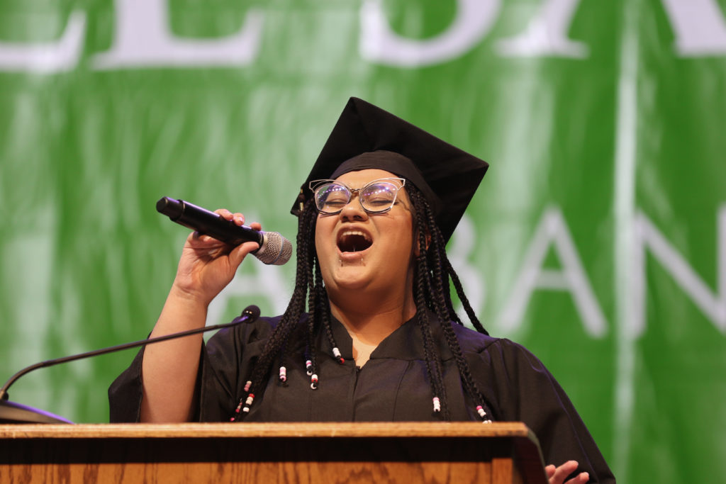 A graduate in cap and gown sings at commencement ceremony