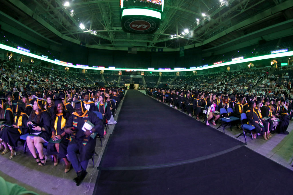 View from front of commencement stage with seated graduates on both sides of carpeted aisle