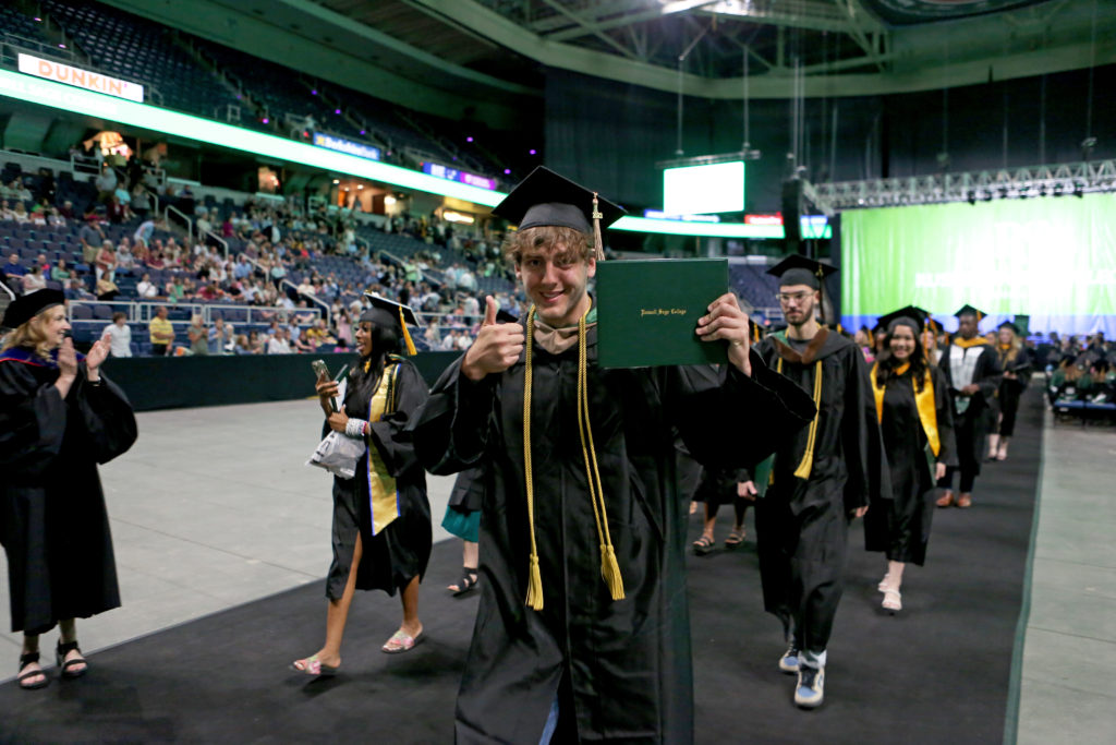 Male graduate in cap and gown holds diploma and gives thumbs up