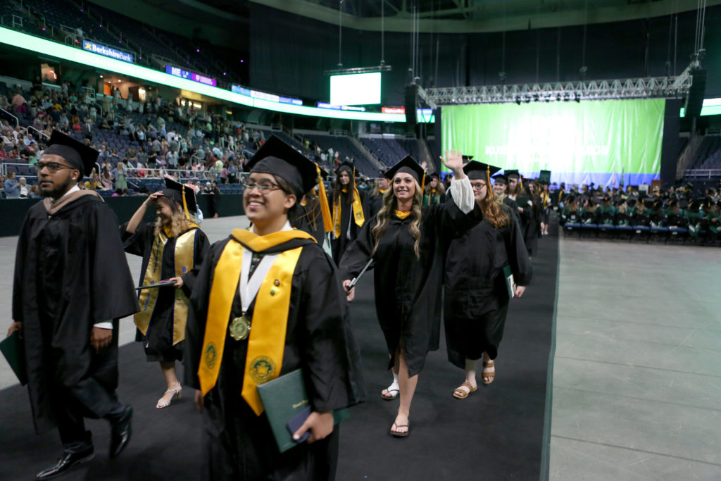 Graduates in cap and gown process with diplomas