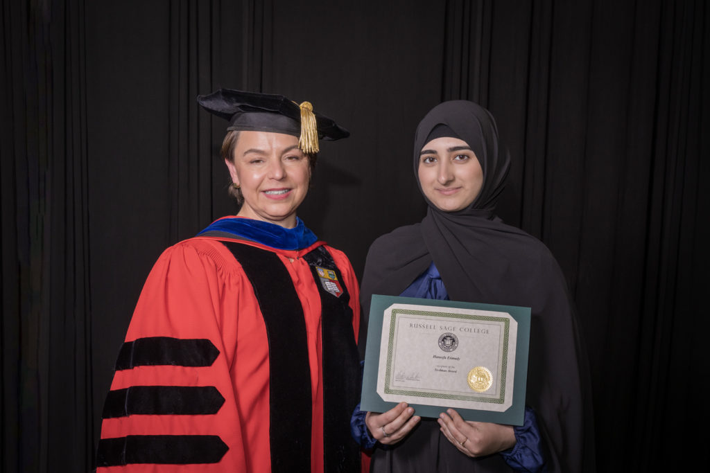 woman in red graduation gown and black hat standing with a female college student with a black hijab holding certificate