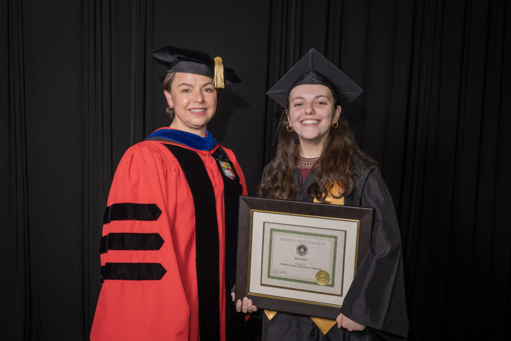 woman in red graduation gown and black hat standing with a female college student also in black commencement gear holding certificate