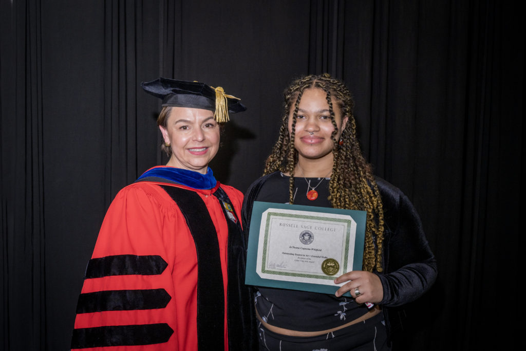 woman in red graduation gown and black hat standing with a female college student with long brown and blond braids holding certificate