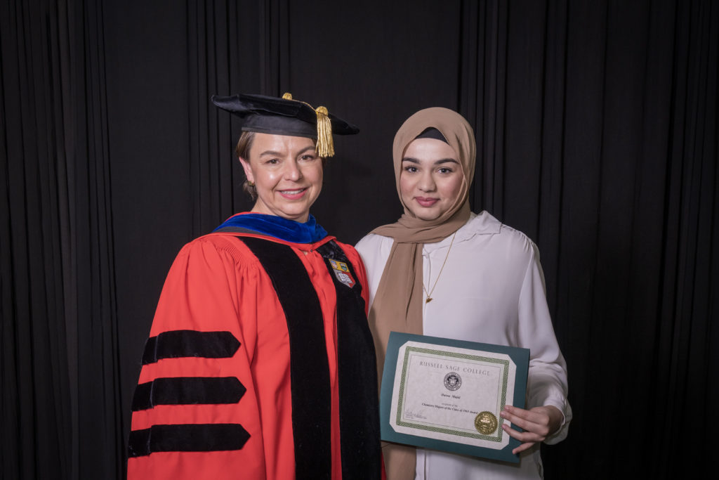 woman in red graduation gown and black hat standing with a female college student in a brown hijab holding certificate