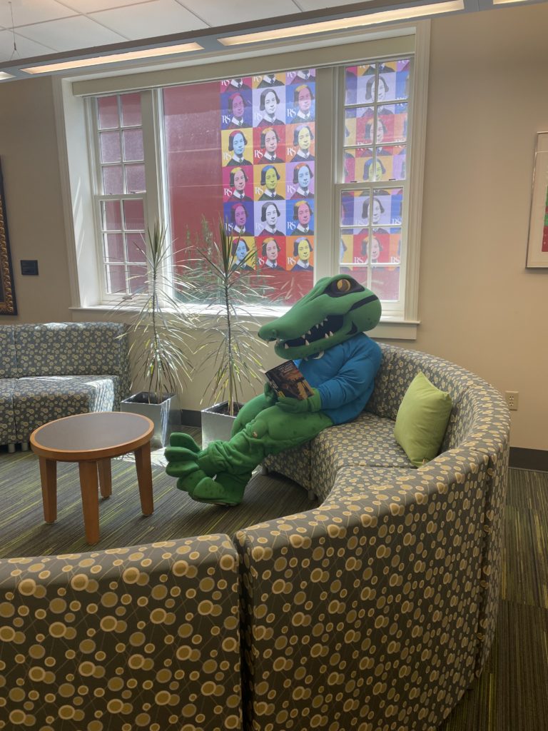 Chompers Mascot reading They Called Us Enemy by George Takei in the Shea Learning Center Library
