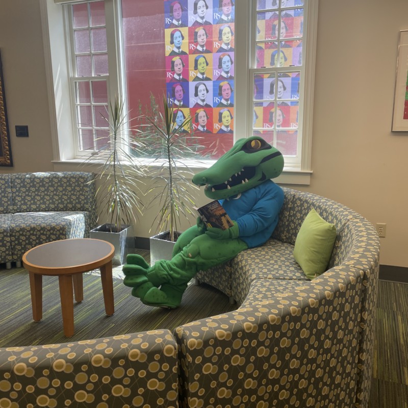 Chompers Mascot reading They Called Us Enemy by George Takei in the Shea Learning Center Library