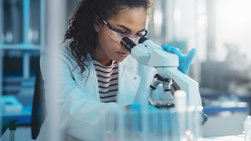 researcher wearing a white lab coat using a microscope