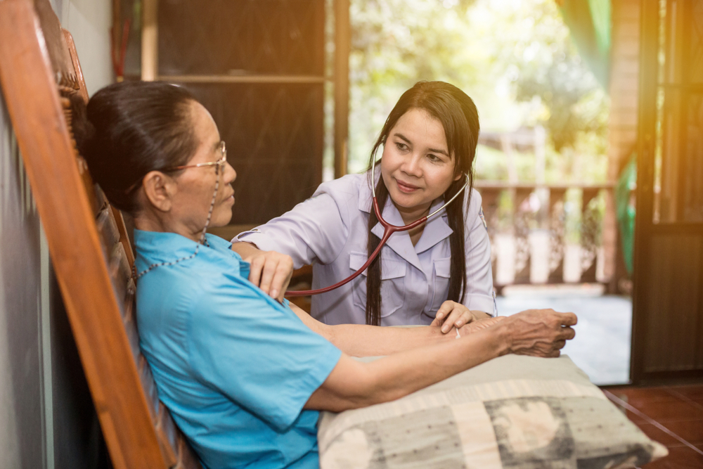 Nurse providing in-home health checks to a seated patient. 