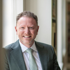person smiling at camera wearing a suit and tie.