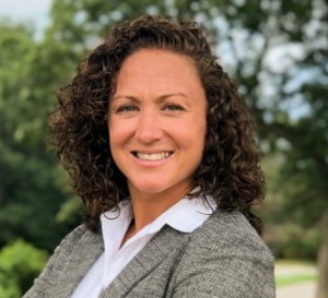 Woman with arms crossed outside smiling at camera dressed in a blazer and dress shirt.