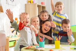 A group of children hug their female teacher in a colorful classroom 