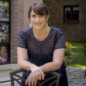 Woman leaning on bench outside smiling at camera