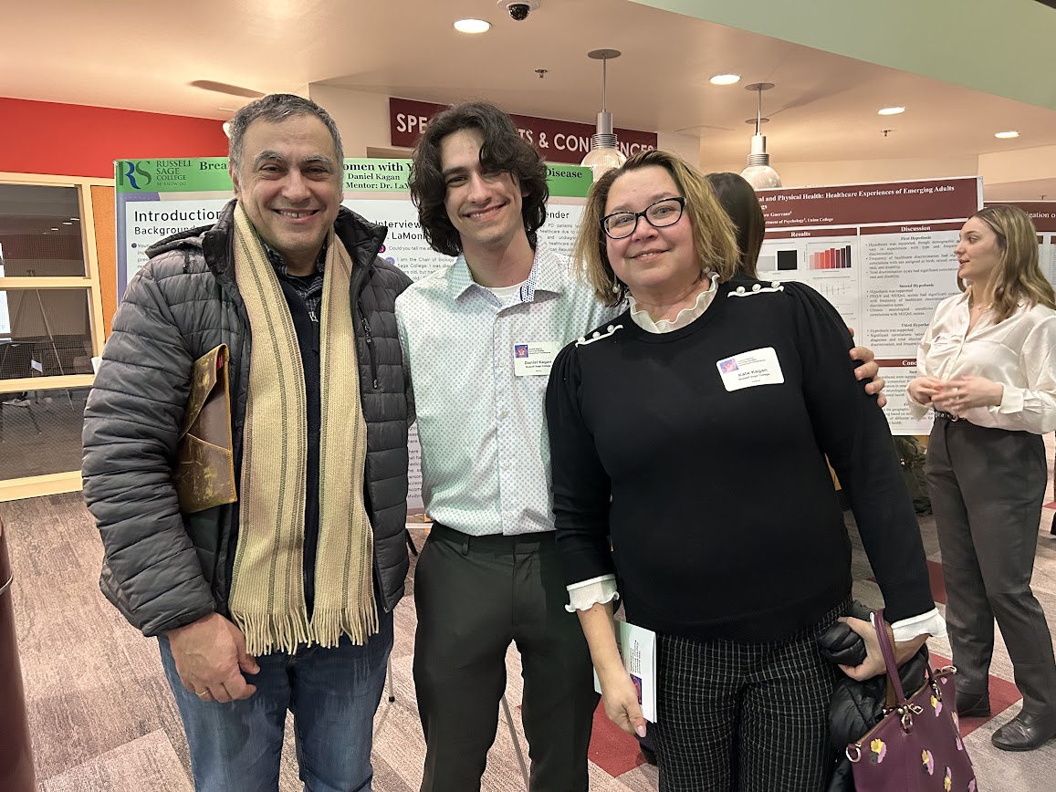 Three people smiling at a conference with poster presentations in the background