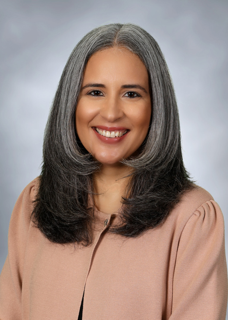 Person with long hair smiling in front of a gray background.
