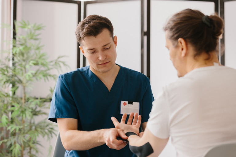 A healthcare professional in blue scrubs applying kinesiology tape to a person's wrist