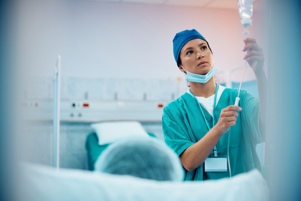 A nurse in surgical scrubs adjusts an IV for a patient, representing hands-on skills in becoming a nurse practitioner.