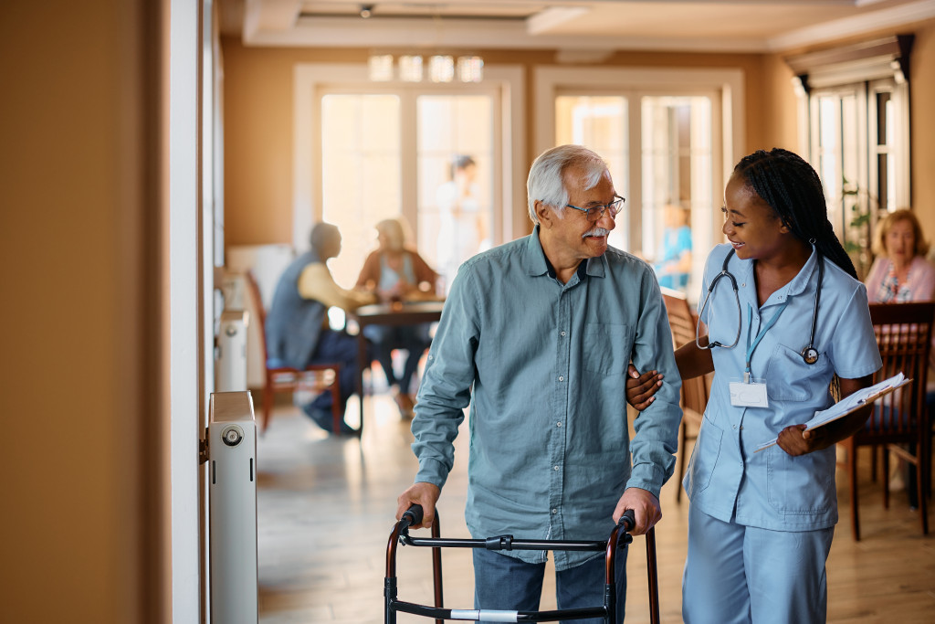 A smiling nurse practitioner helps an elderly patient using a walker, showing a real-world nursing career in action.
