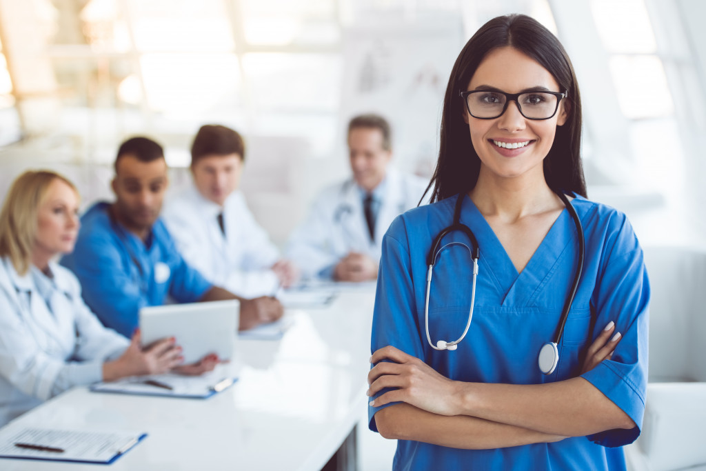 A confident nurse in scrubs smiles with a medical team in the background, representing a path to becoming an RN