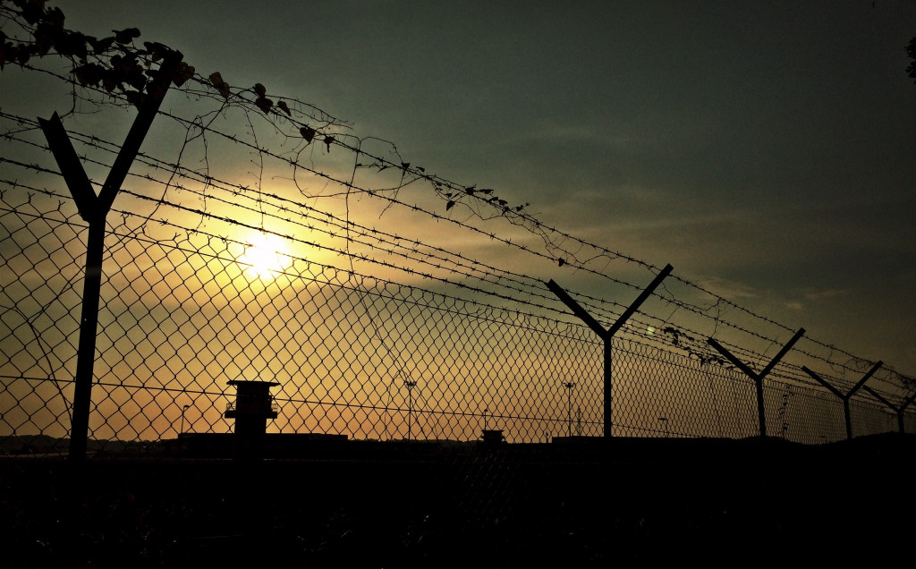 Barbed wire fence with guard towers silhouetted against the sunset, representing corrections and incarceration in the criminal justice field.