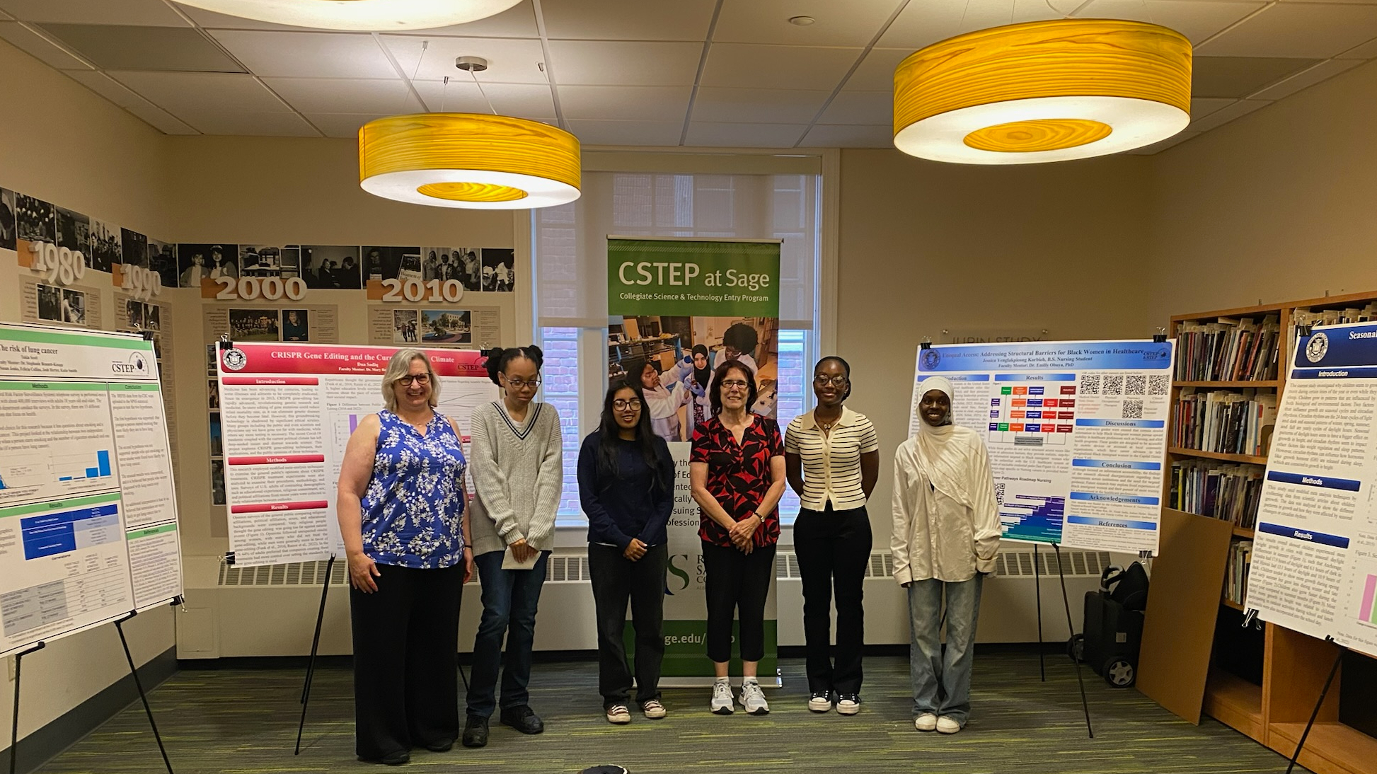 Six people stand in front of research posters and a banner in a library setting