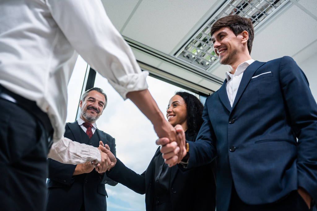 A business meeting with two people shaking hands, while two others smile in the background