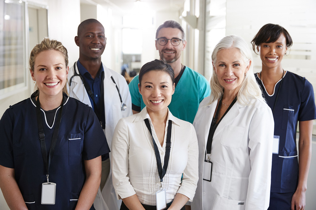 A diverse group of healthcare professionals smiling in a hospital corridor, wearing name badges.