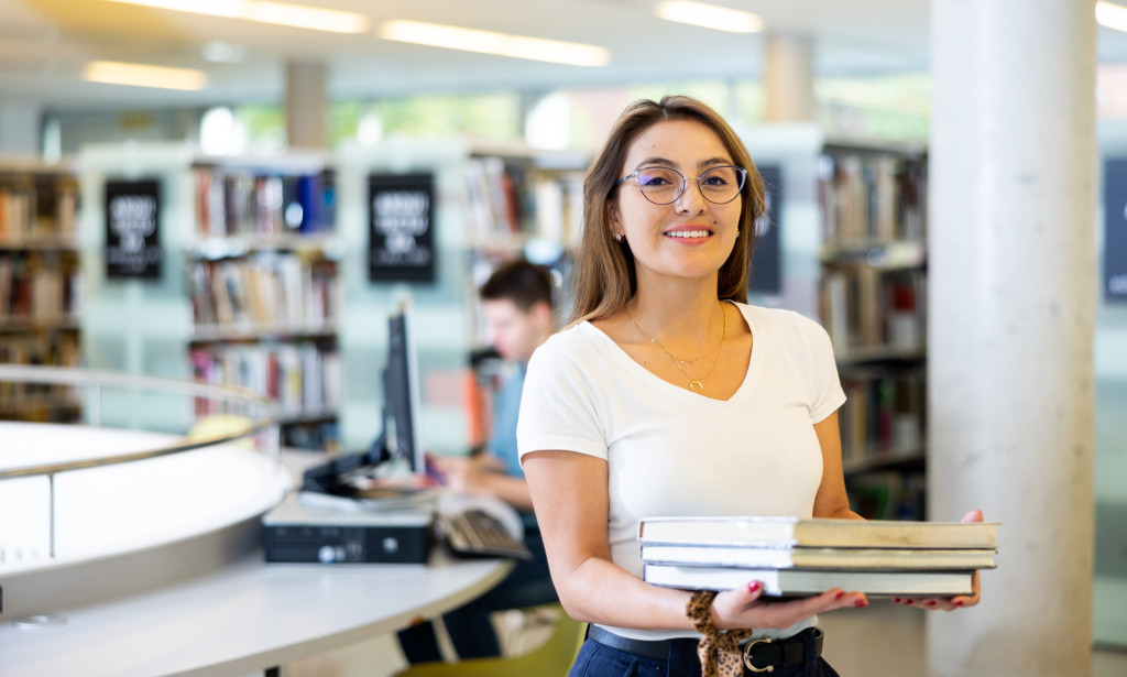 Student in library preparing for graduate school, researching master’s degree requirements and programs
