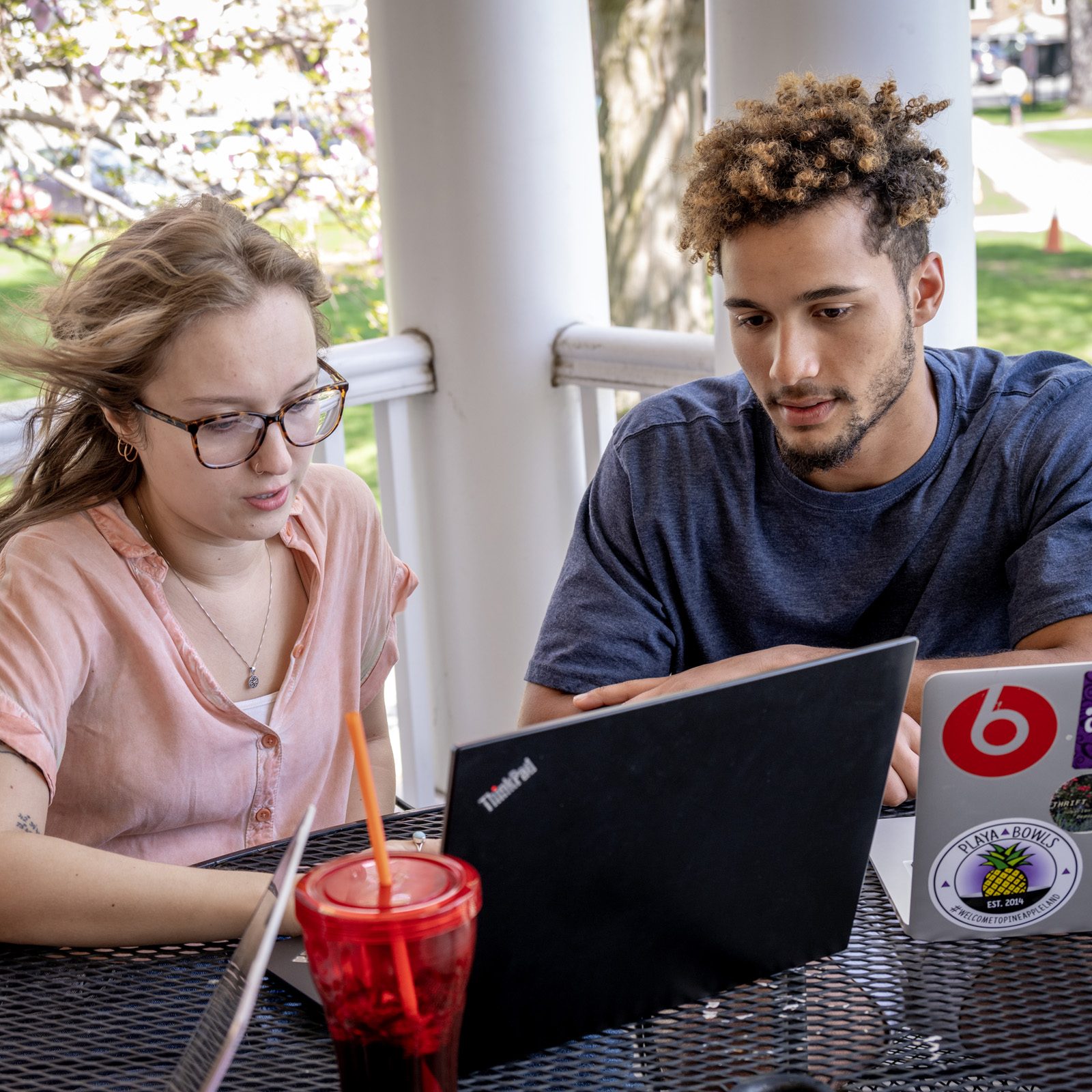 Two people gathered around two laptop computers at a table outside.