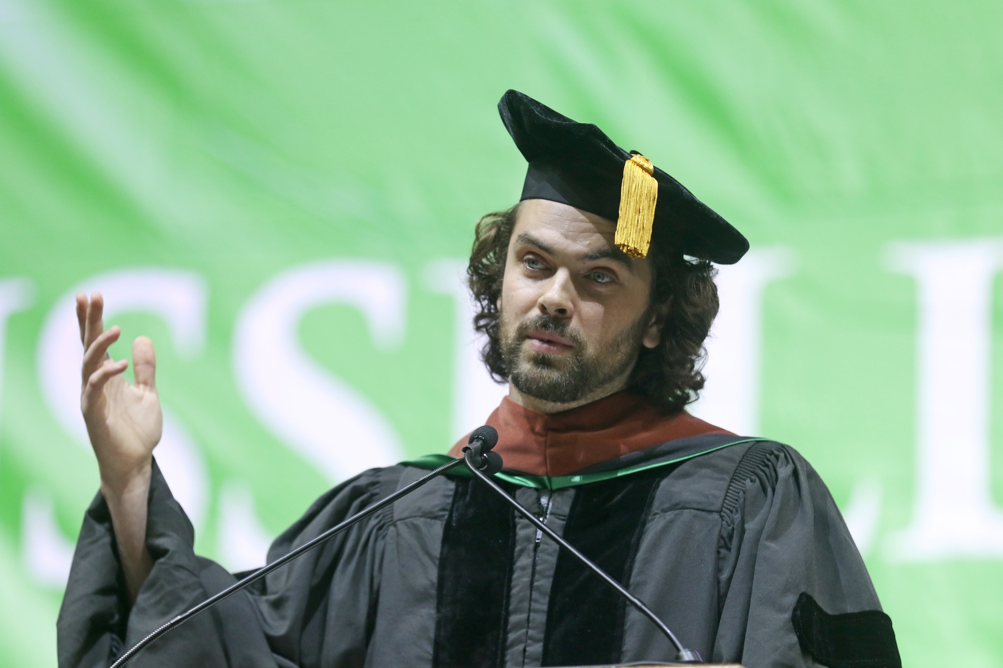 Actor Lucas Aurelio stands at podium dressed in cap and gown at Russell Sage College 2025 commencement ceremony.
