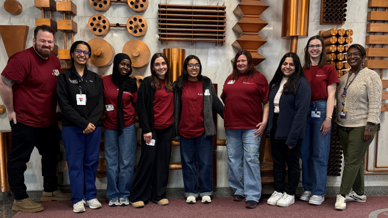 nine people stands in front of a wall with abstract copper designs