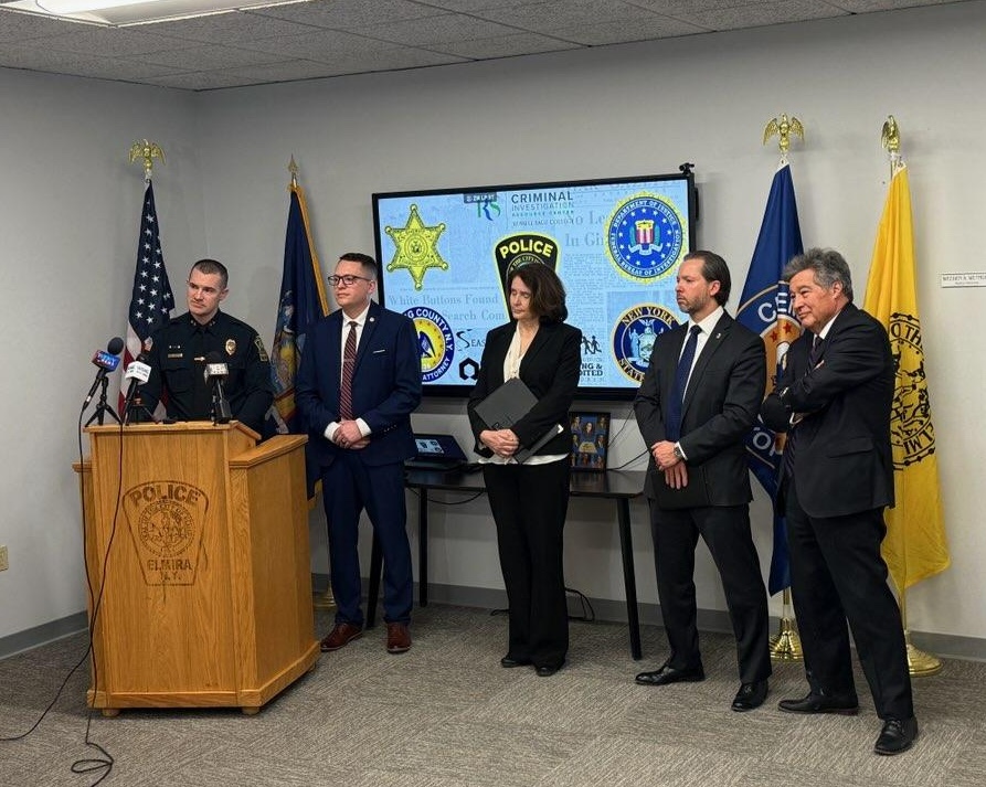 police officer behind podium with line of four people dressed professionally beside him.