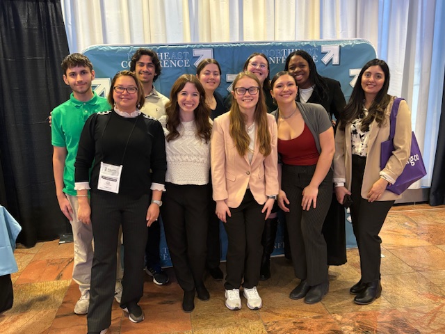 10 people poses in front of a blue conference backdrop, all smiling