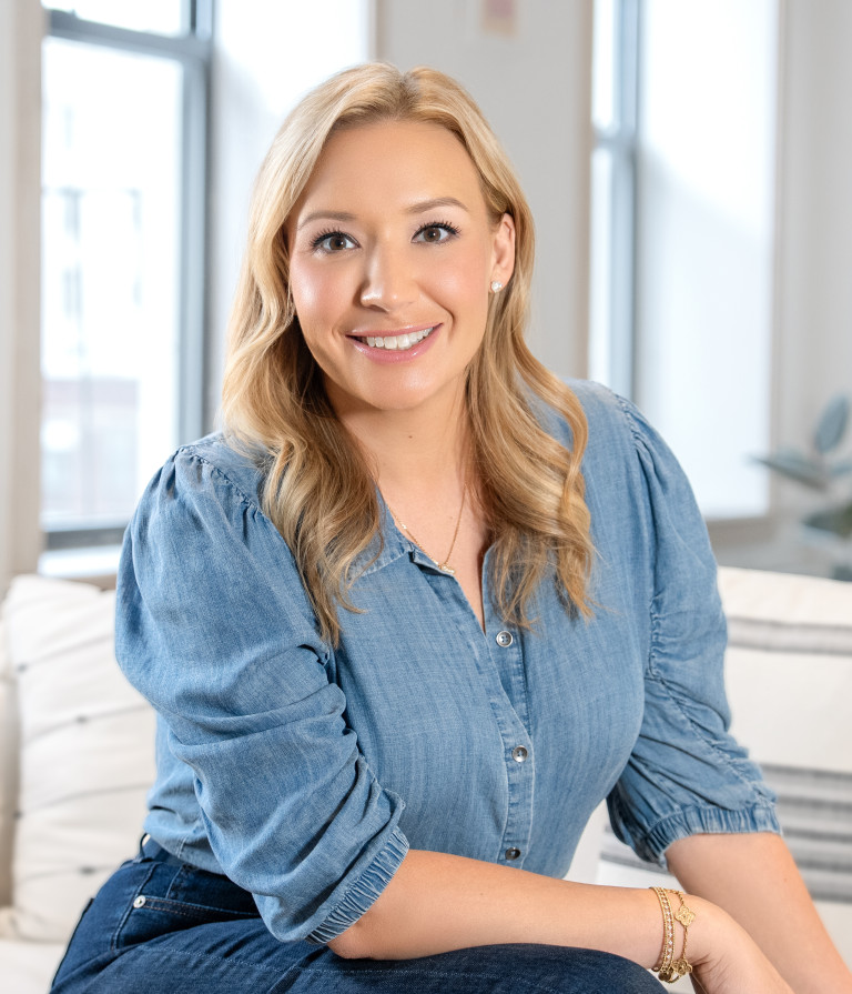 woman dressed in blue seated and smiling at the camera indoors.