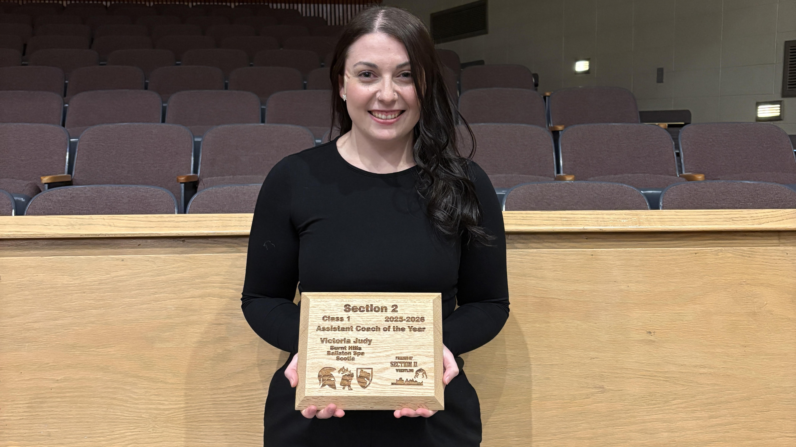 Victoria Judy holding a wooden plaque in an empty auditorium.