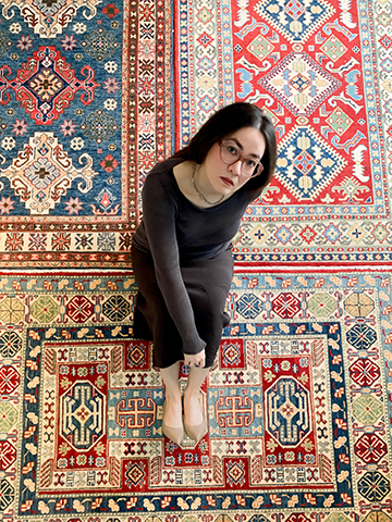 A person with glasses sitting on a colorful, patterned carpet, looking upwards.