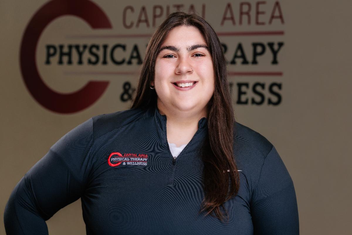 Person smiling, wearing a dark gray top with a physical therapy logo