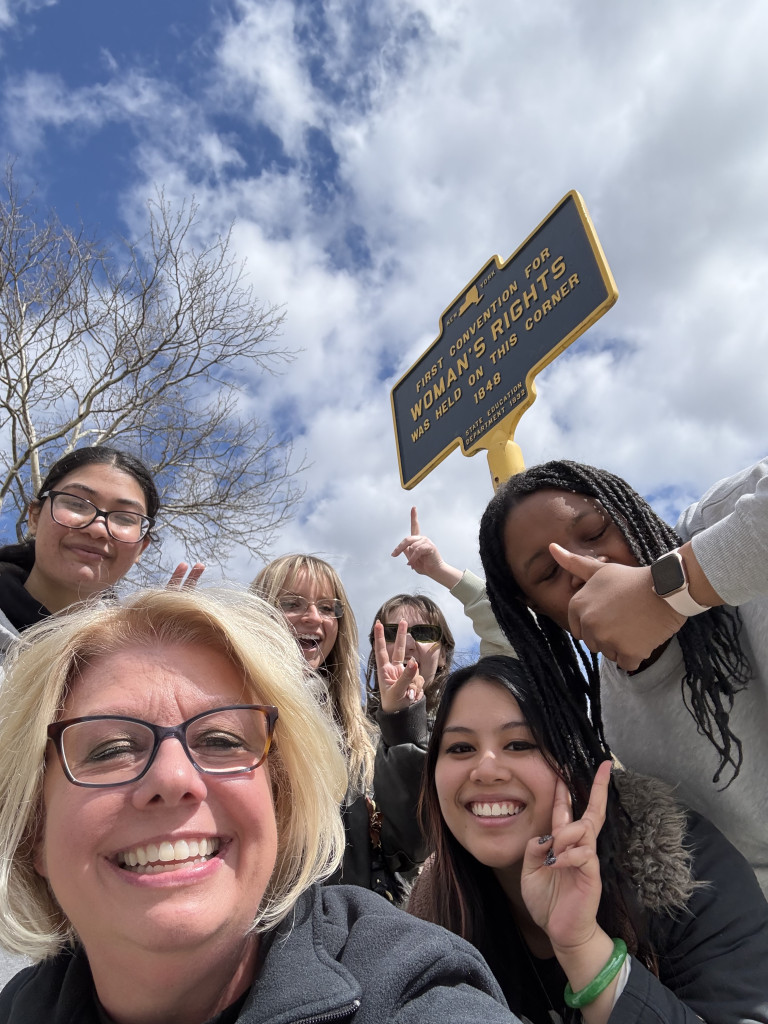 Women ambassadors and RSC Alumnaei smiling for group selfie at Seneca Falls on April 11 in the Women’s Rights National Historic Park