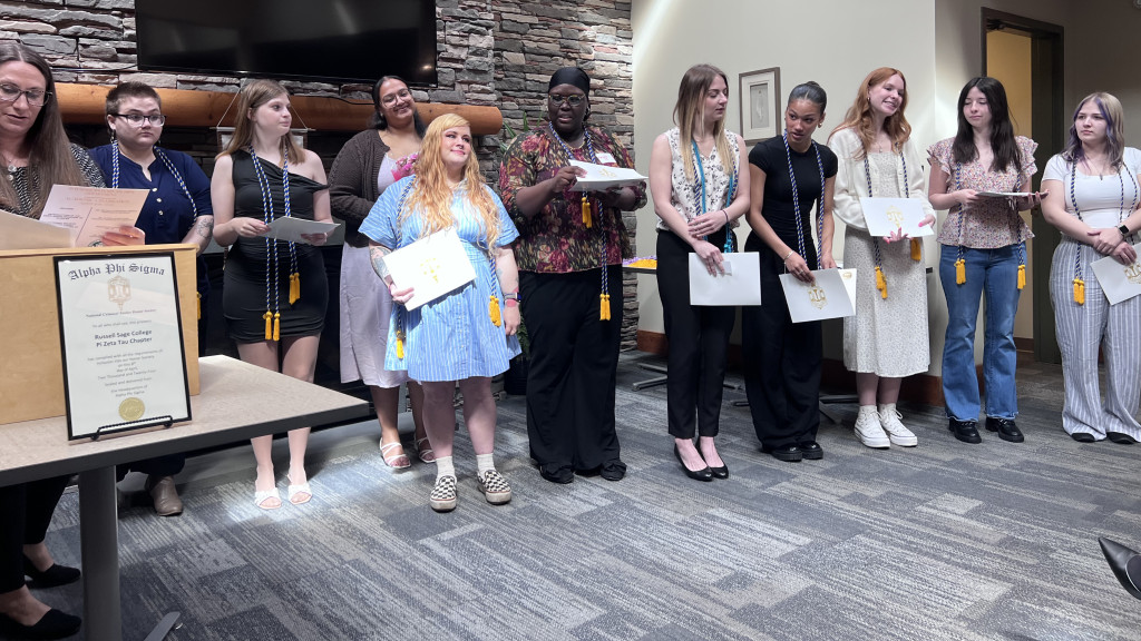 A group of people with honor cords hold certificates in a ceremony setting.