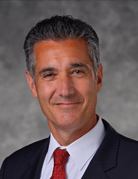 man dressed professionally smiling at the camera with gray background