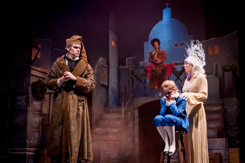 three people in costume on stage. one dressed like scrooge, one little girl, and one ghost of christmas past