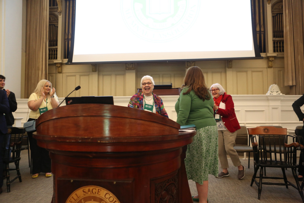 Women gathered around podium in auditorium smiling and laughing