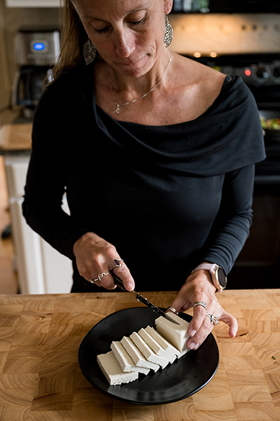 Nutrition Professor slicing tofu onto a black plate in a kitchen