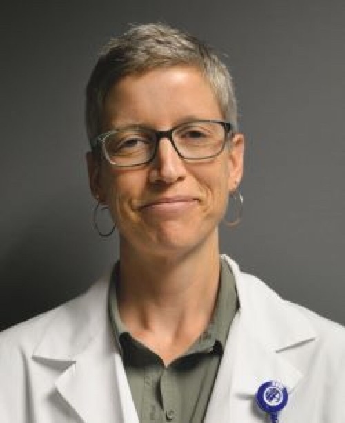 Woman in white lab coat and glasses smiling at camera